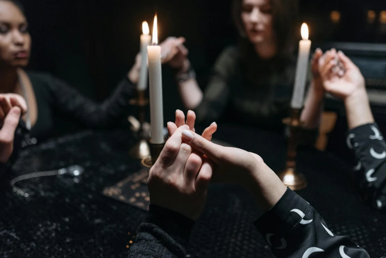 a group of people sitting around a table holding candles, by Julia Pishtar, trending on pexels, witch clothes, holding hands, holding nevermore, instagram post