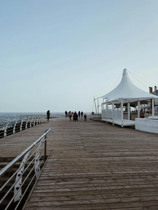 a white tent sitting on top of a pier next to the ocean, people walking around, surrounding the city, jovana rikalo, low quality photo