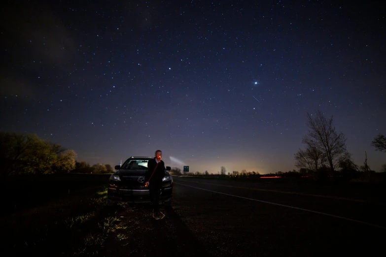 a man standing on the side of a road next to a car, by Adam Pijnacker, underneath the stars, andrei ryabovichev, portait image