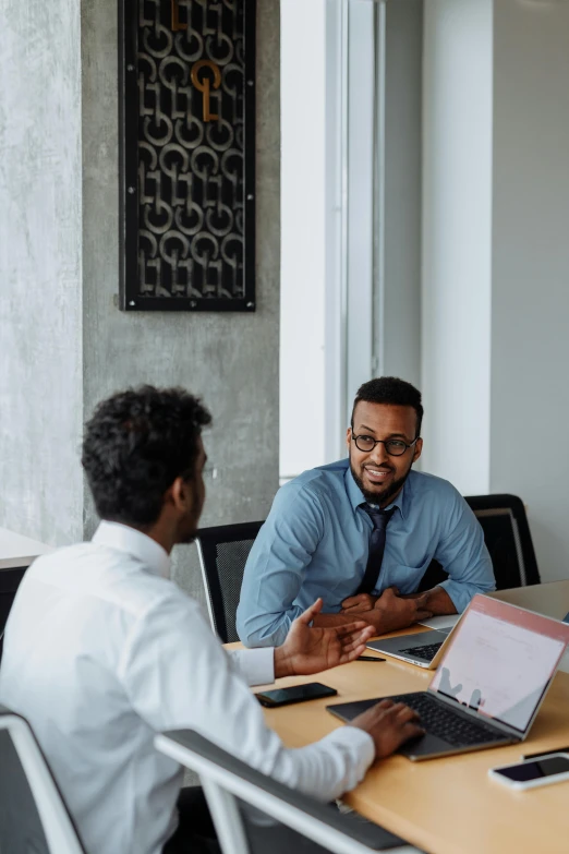 a group of people sitting around a table with laptops, two men, wearing business casual dress, riyahd cassiem, thumbnail