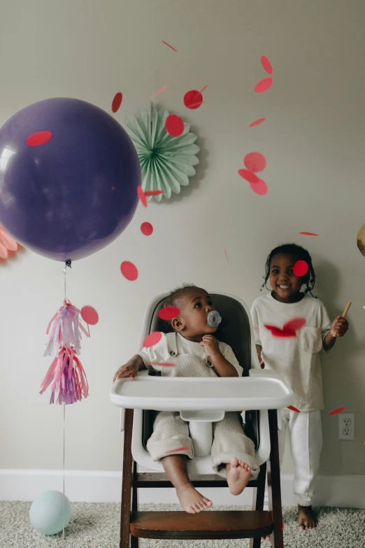 a couple of kids that are sitting in a high chair, by Dulah Marie Evans, pexels contest winner, process art, party balloons, purple themed, dwell, ( ( dark skin ) )