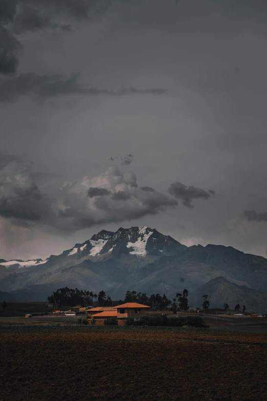 a field with a mountain in the background, unsplash contest winner, quito school, dark stormy weather, neo - andean architecture, evening storm, mountain snow