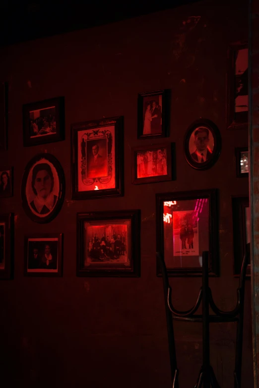 a room that has a bunch of pictures on the wall, inspired by Gertrude Abercrombie, holography, soft red lights, 1 9 2 0's style speakeasy, demonic photograph, photos of family on wall