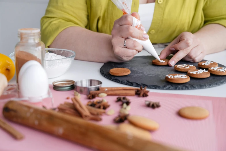 a woman is decorating cookies on a table, by Julia Pishtar, professional product photo, round format, decoration, easy to use