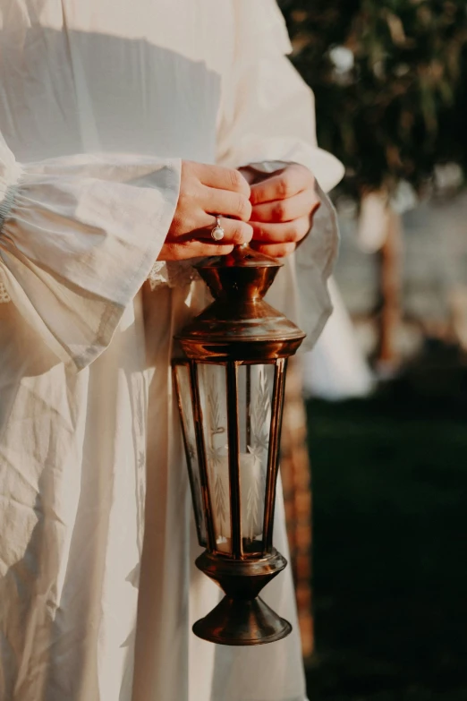 a woman in a white dress holding a lantern, unsplash, ivory and copper, ring lit, wearing robe, wedding