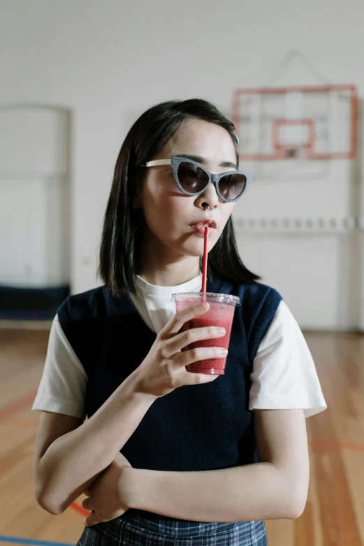 a woman holding a drink with a straw in her hand, an album cover, inspired by Fei Danxu, trending on pexels, in the high school gym, wearing shades, berry juice, still frame from a movie