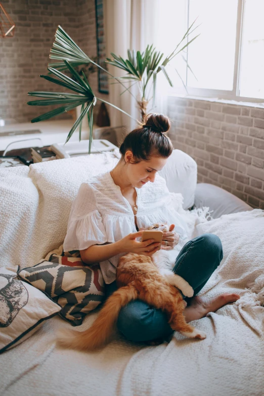 a woman sitting on a bed with a cat, pexels contest winner, tending on pinterest, topknot, on a couch, sydney hanson