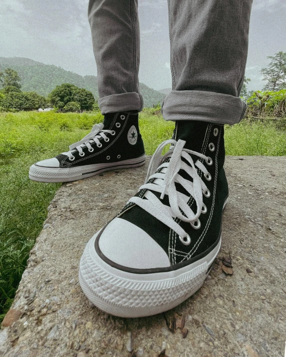 a person standing on a rock wearing black and white converses, trending on pexels, photorealism, sitting on green grass, product introduction photo