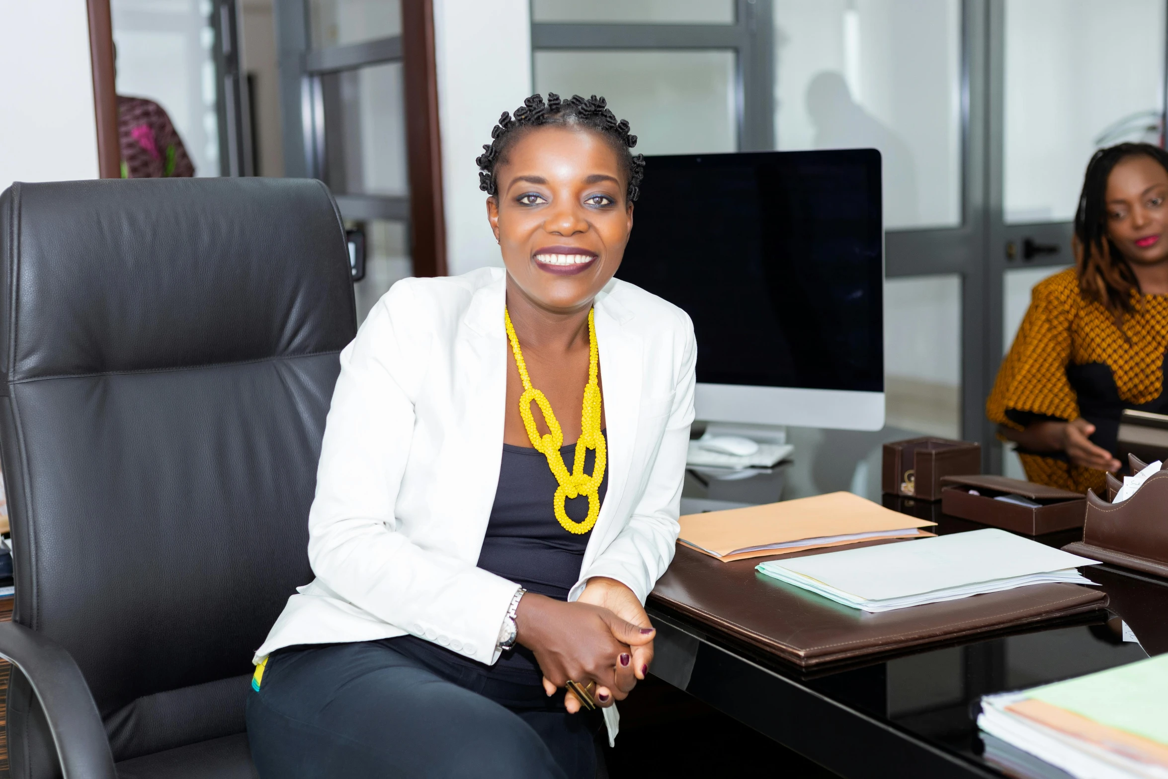 a woman sitting at a desk in front of a computer, by Chinwe Chukwuogo-Roy, pexels contest winner, woman in business suit, lady using yellow dress, confident smirk, mongezi ncaphayi