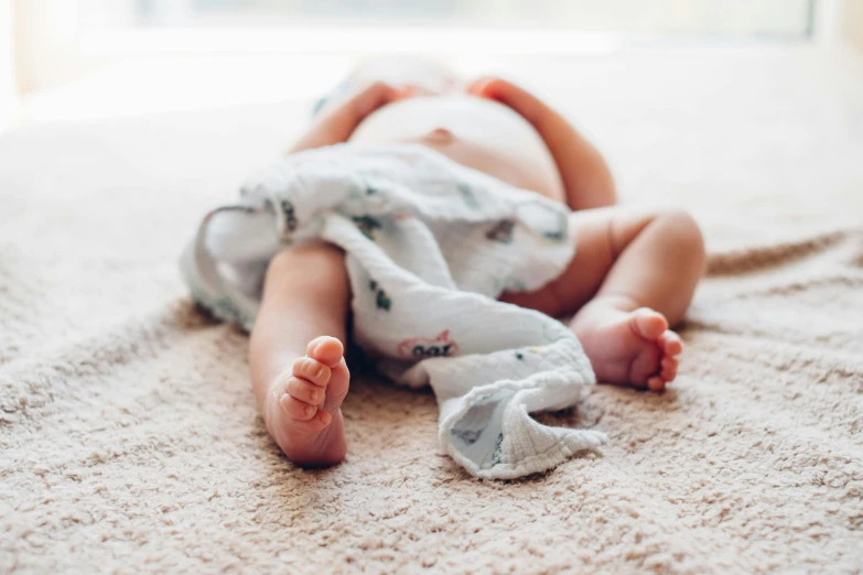 a baby laying on its back on the floor, by Daniel Lieske, pexels contest winner, wearing a towel, thighs close up, folded, fertility