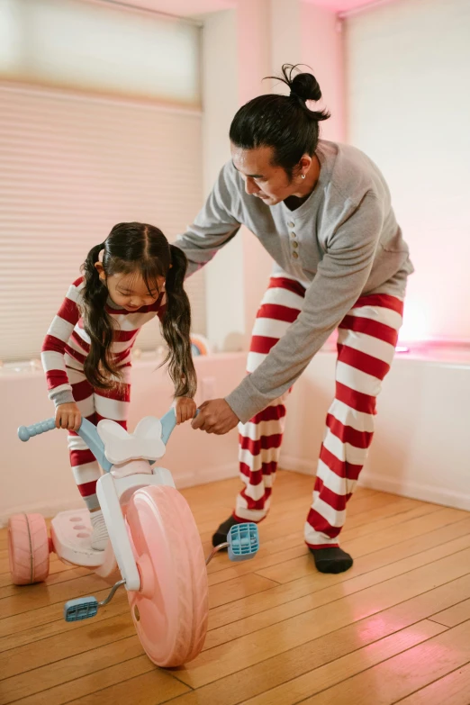 a woman teaching a little girl how to ride a bike, inspired by The Family Circus, pexels contest winner, process art, wearing pajamas, asian man, candy canes, daddy/fatherly