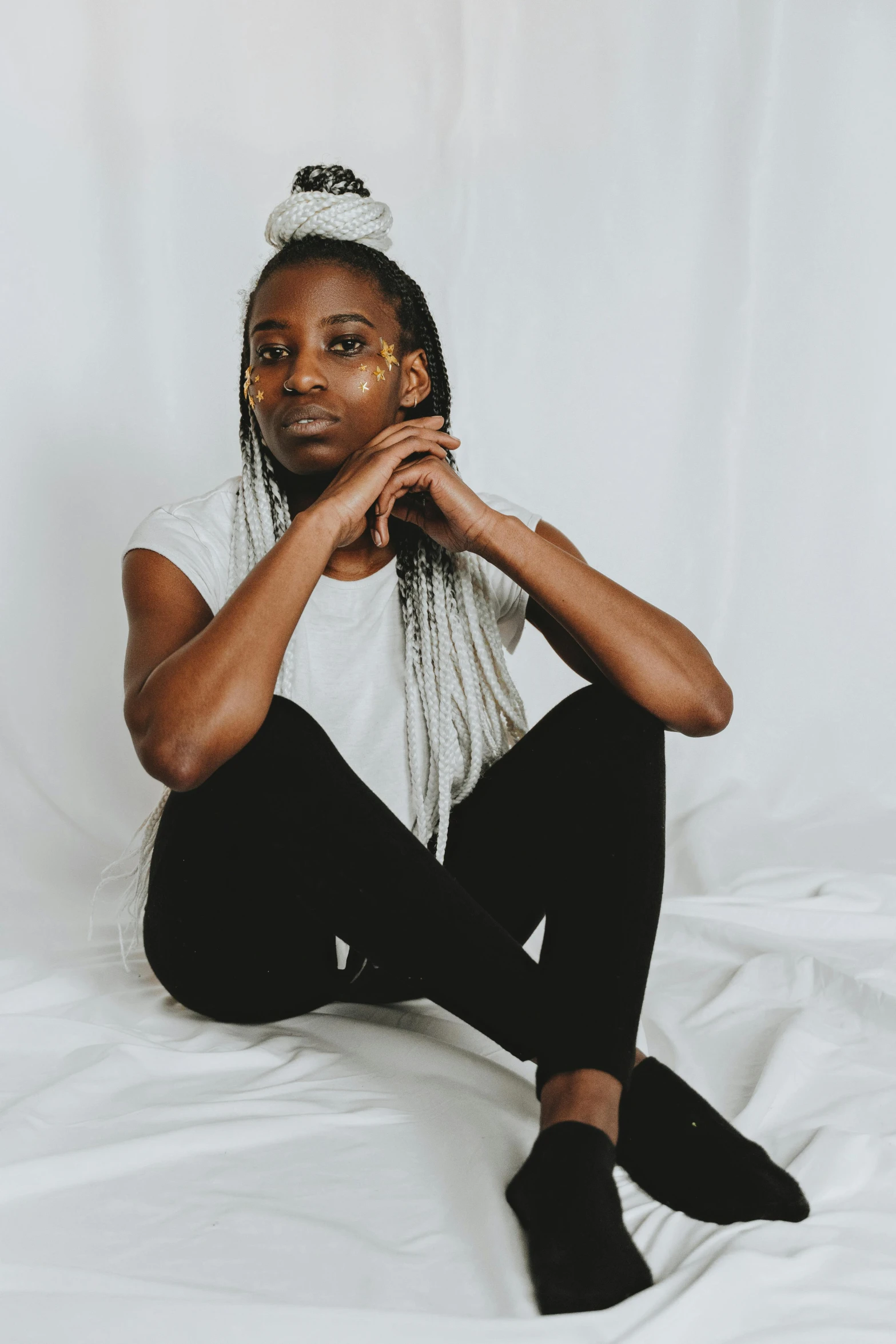 a woman with dreadlocks sitting on a bed, trending on pexels, black arts movement, wearing pants and a t-shirt, non-binary, plain background, gray skin