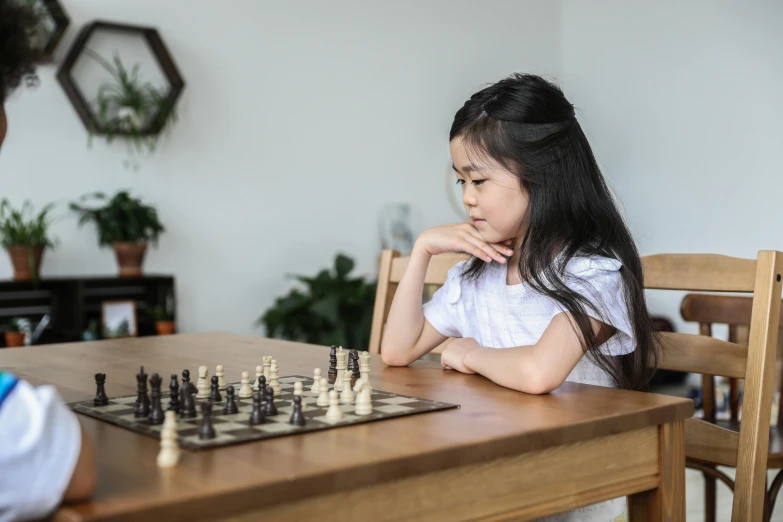 a little girl sitting at a table playing a game of chess, pexels contest winner, 15081959 21121991 01012000 4k, asian female, profile picture 1024px, high quality image