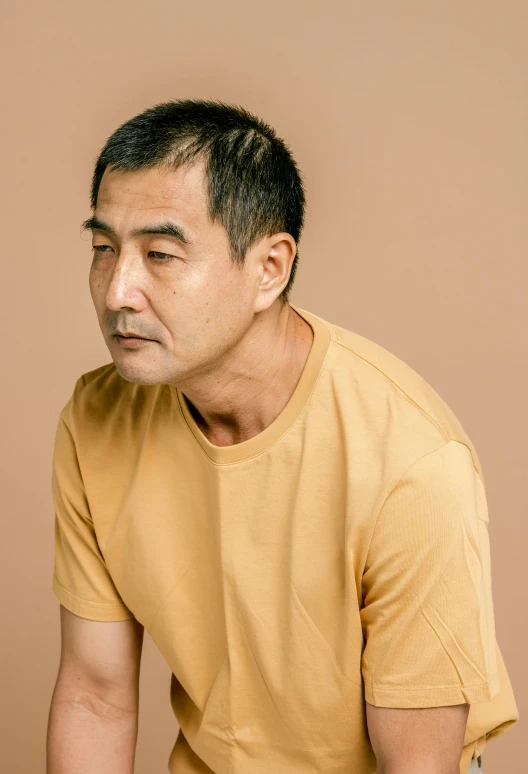 a man in a yellow shirt holding a remote control, inspired by Kanō Naizen, trending on unsplash, shin hanga, studio portrait, joe taslim, pensive, wearing a brown