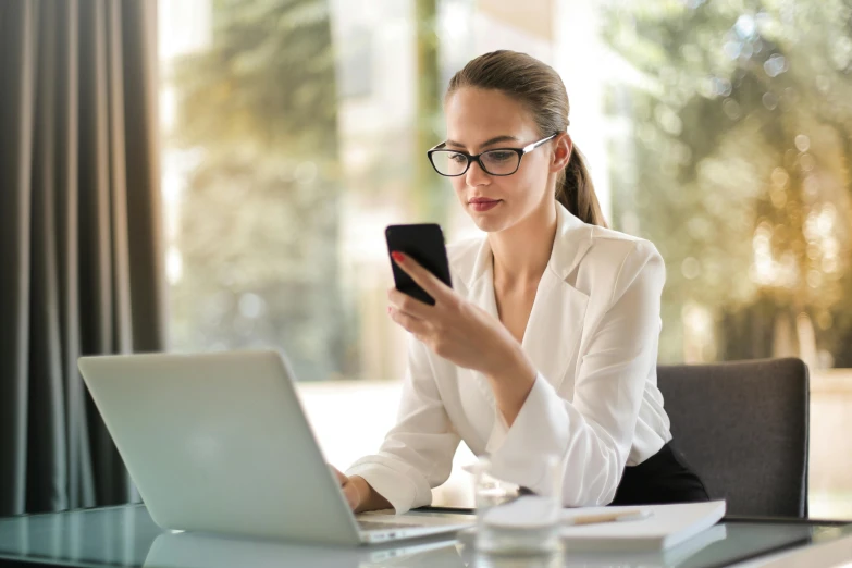 a woman sitting at a table using a cell phone, wearing black rimmed glasses, worksafe. instagram photo, computer screens, female lawyer