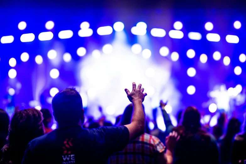 a crowd of people at a concert with their hands in the air, pexels, church background, fan favorite, bursting with blue light, holding his hands up to his face