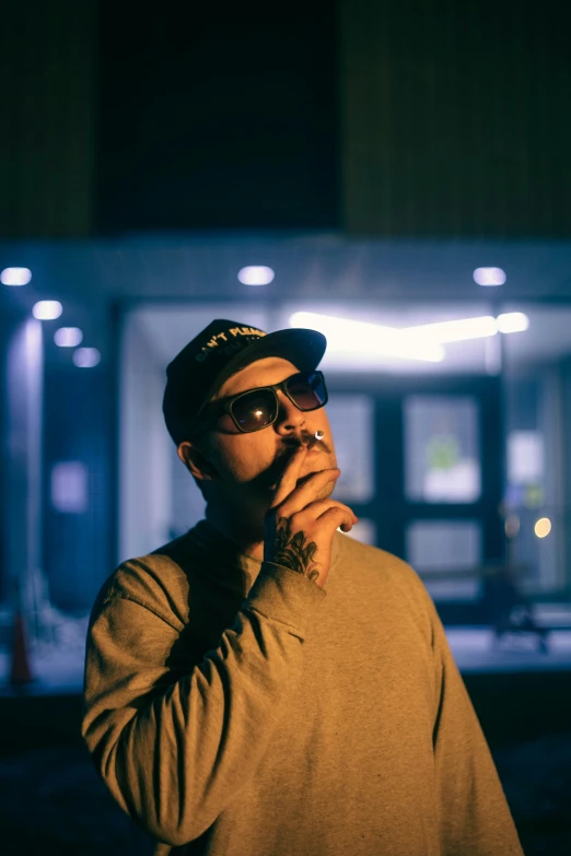 a man standing in front of a building smoking a cigarette, mac miller, light from right, shades, thoughtful