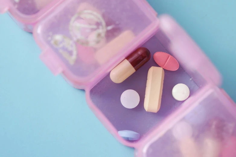 a close up of a plastic container filled with pills, by Rachel Reckitt, trending on pexels, antipodeans, blue and pink, a wooden, finely illustrated, bandages