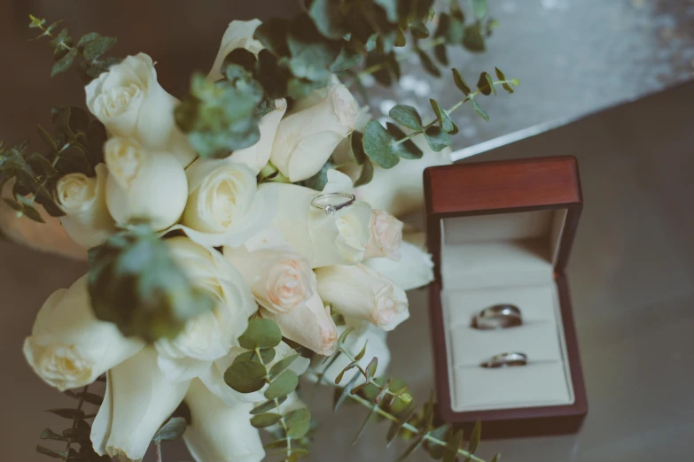 a bouquet of white roses and two wedding rings, a still life, trending on unsplash, on a table, **cinematic, various items, commercially ready