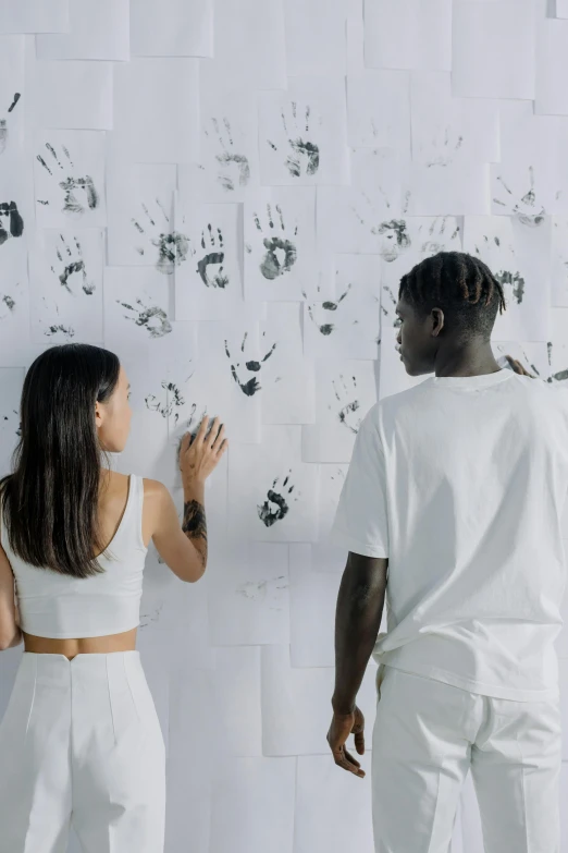 a man and a woman standing in front of a wall, a silk screen, trending on unsplash, black arts movement, thumbprint, on a white table, human hands, white ink