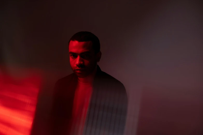 a man standing in front of a red light, an album cover, pexels contest winner, moody dim faint lighting, ahmad merheb, portrait of mario, glowing with colored light