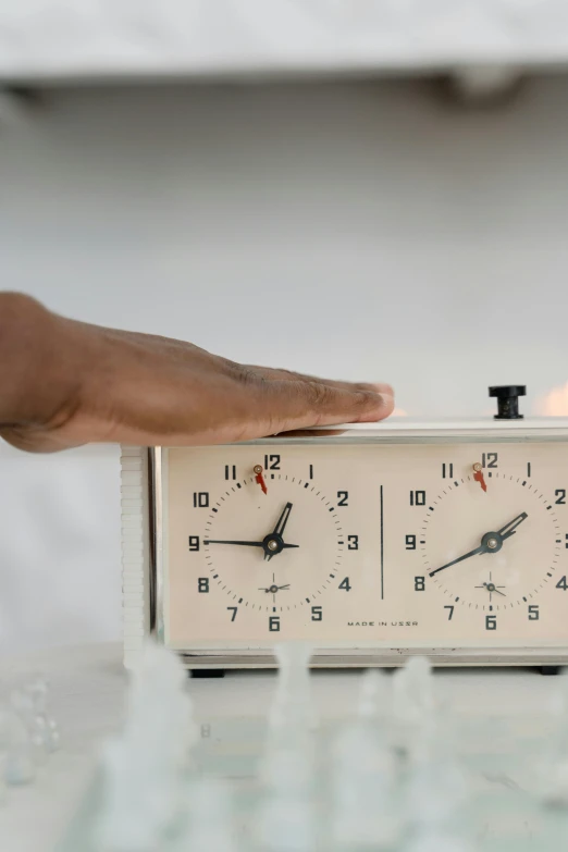 a white alarm clock sitting on top of a table, an album cover, by Matija Jama, unsplash, kinetic art, hands on counter, historical, freezing, holding a candle