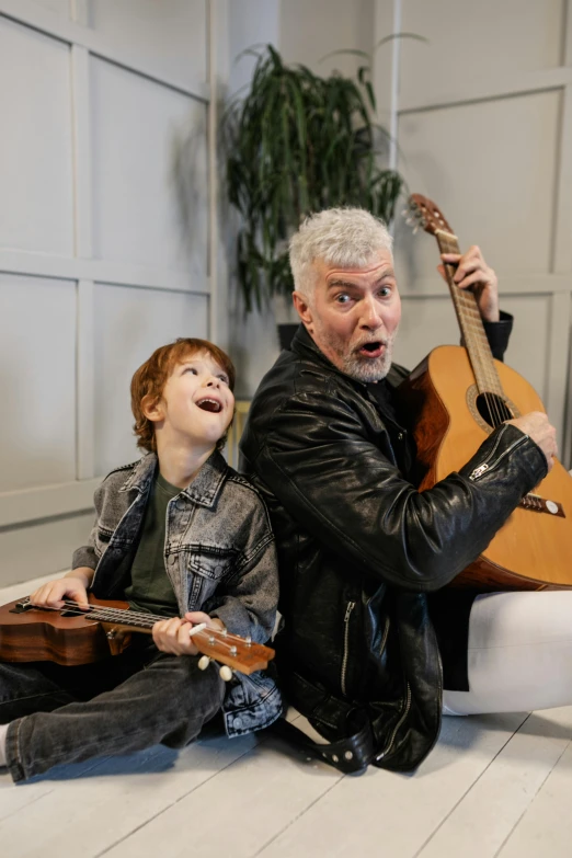 a man sitting next to a little boy holding a guitar, inspired by Phil Foglio, gray haired, press photo, youtube thumbnail, actors