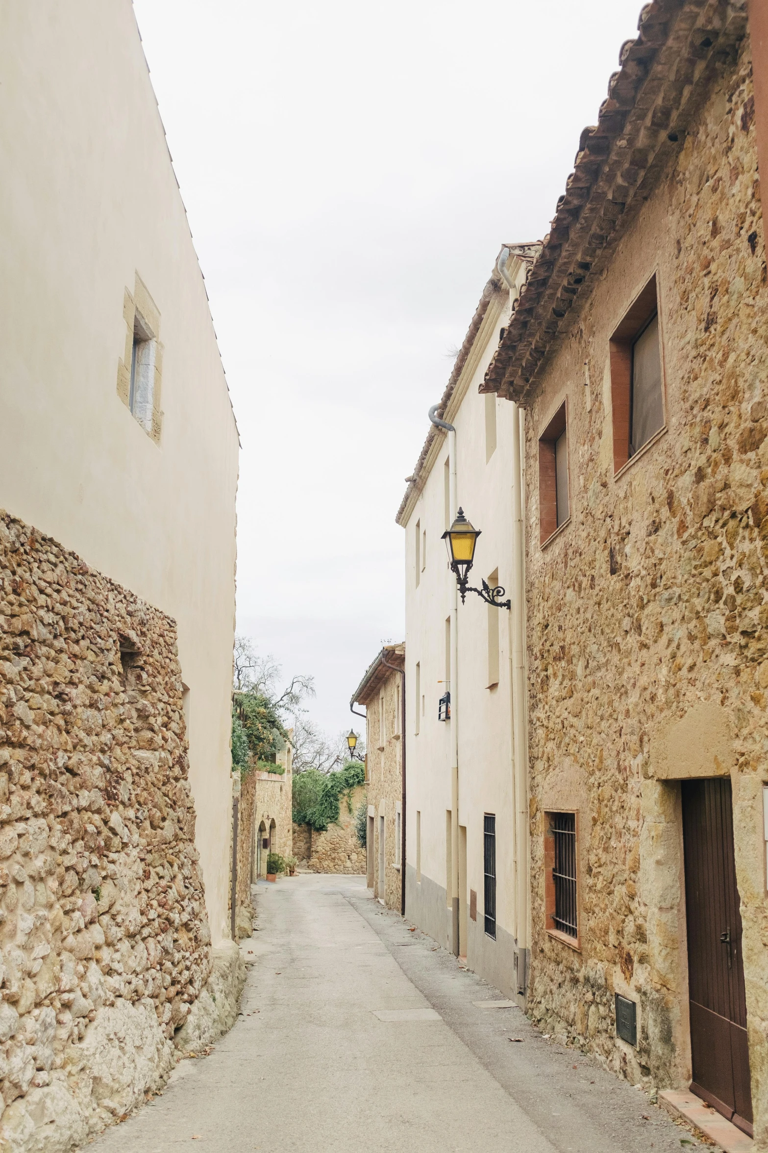 a narrow street is lined with stone buildings, costa blanca, classic vibes, countryside, streetlamps