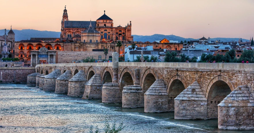 a bridge over a river with a castle in the background, moorish architecture, in the golden hour, geodesic domes, travel guide