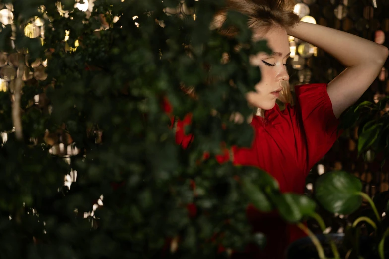 a woman in a red shirt standing next to a bush, trending on pexels, romanticism, sydney sweeney, hiding, concept photo, portrait image