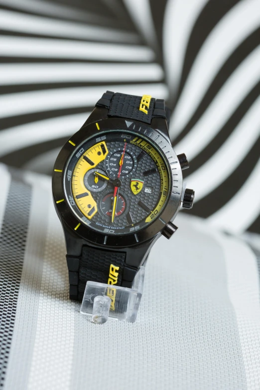 a close up of a watch on a table, inspired by Francesco Furini, pop art, black armor with yellow accents, ferrari logo on it's chest, thumbnail, 0