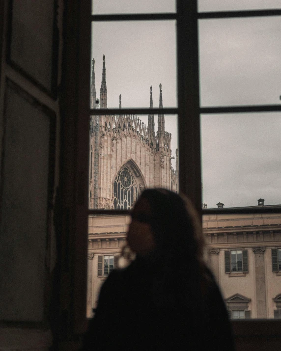 a woman looking out a window at a cathedral, inspired by René Burri, pexels contest winner, lesbians, milan jozing, seen from a distance, gothic library