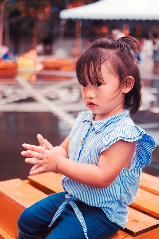 a little girl sitting on top of a wooden bench, inspired by Ni Duan, pexels contest winner, interactive art, spinning hands and feet, annoyed, square, jakarta