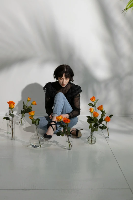 a woman sitting on the floor surrounded by vases of flowers, an album cover, trending on pexels, realism, finn wolfhard, full body photogenic shot, concert photo, in front of white back drop