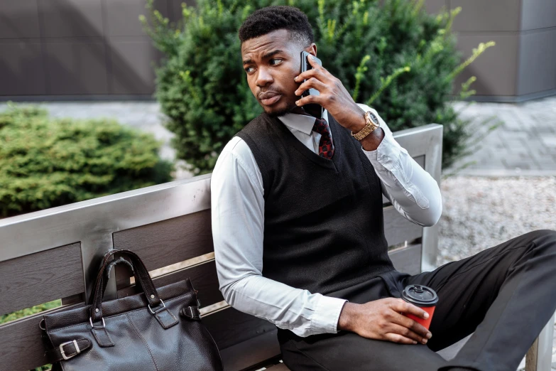 a man sitting on a bench talking on a cell phone, wearing a vest and a tie, man is with black skin, 2019 trending photo, attractive man drinking coffee