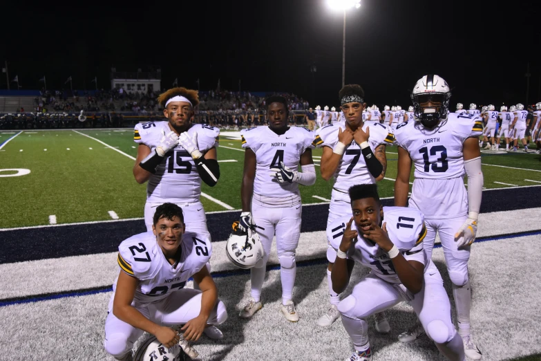 a group of men standing next to each other on a field, white + blue + gold + black, high school, set at night, captain