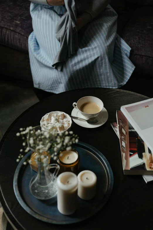 a woman sitting on a couch talking on a cell phone, two cups of coffee, white candles, sitting on a mocha-colored table, curled up on a book