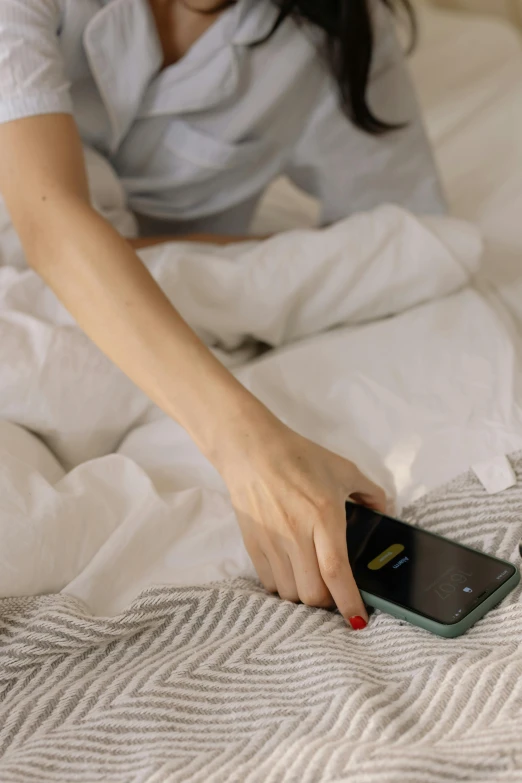 a woman sitting on a bed holding a cell phone, trending on pexels, un made bed, 6 : 3 0 am, vibrating, trending on dezeen