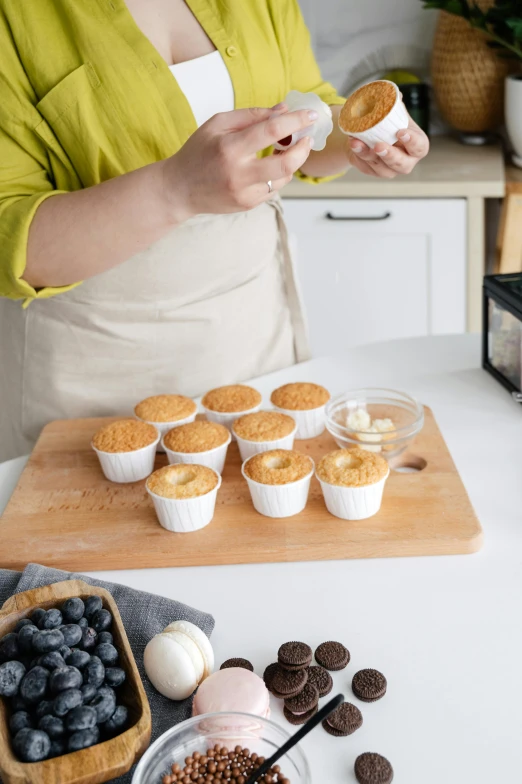 a woman standing in a kitchen preparing cupcakes, inspired by Wilhelm Hammershøi, unsplash, photorealism, official product photo, wood cups, vanilla, with a soft