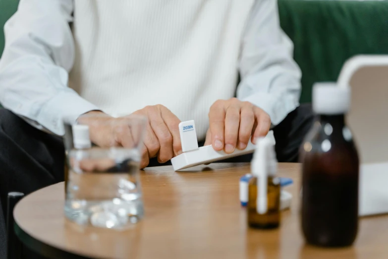 a man sitting at a table in front of a laptop, pills and medicine, subtle detailing, holding a bottle of arak, profile image