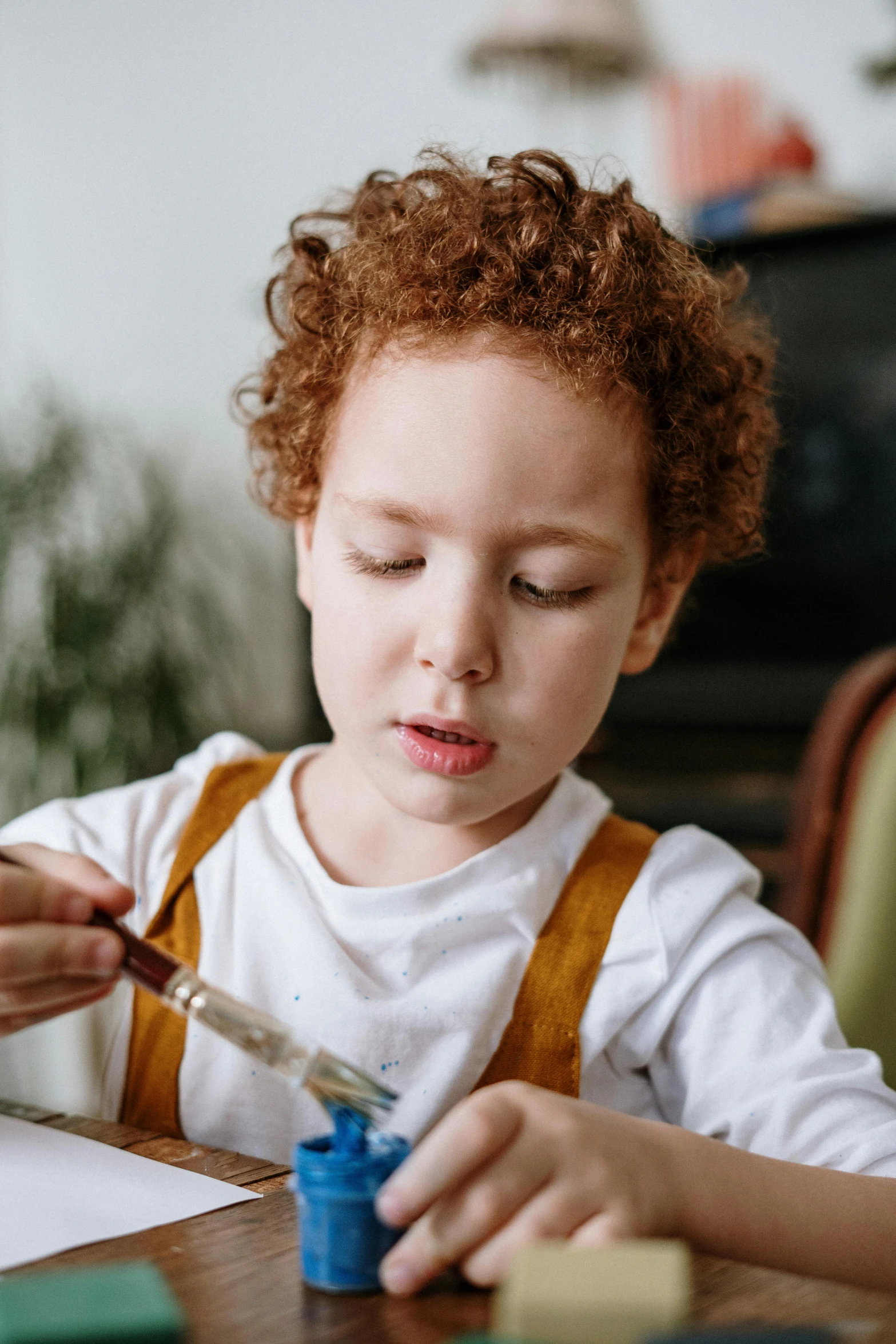 a little boy that is sitting at a table, pexels contest winner, process art, holding a paintbrush, red haired teen boy, brown and white color scheme, gif