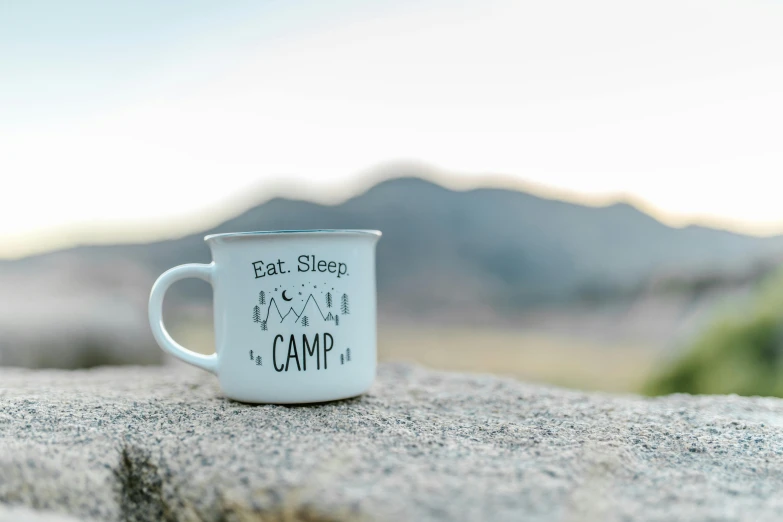 a white coffee cup sitting on top of a rock, a photo, summer camp, grey, high quality product image”, front shot