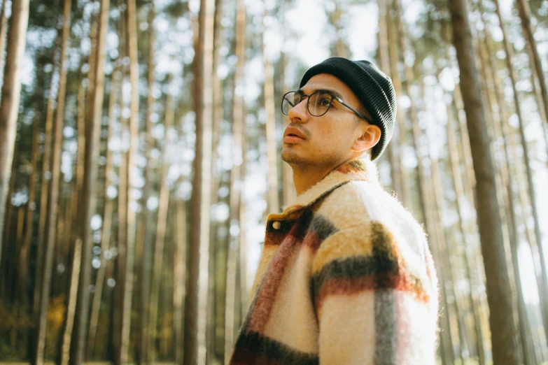 a man standing in the middle of a forest, an album cover, trending on pexels, in square-rimmed glasses, he wears a big coat, andrew gonzalez, looking to the side off camera