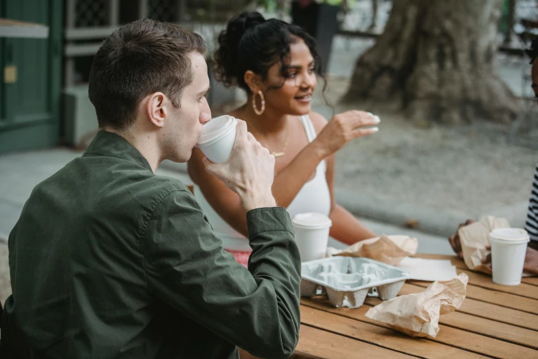 a group of people sitting around a wooden table, next to a cup, sitting on a park bench, background image, profile pic