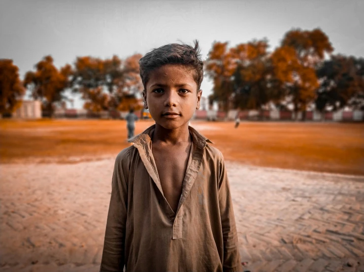 a young boy standing on top of a sandy field, by Riza Abbasi, pexels contest winner, handsome face, standing in township street, a park, professionally color graded