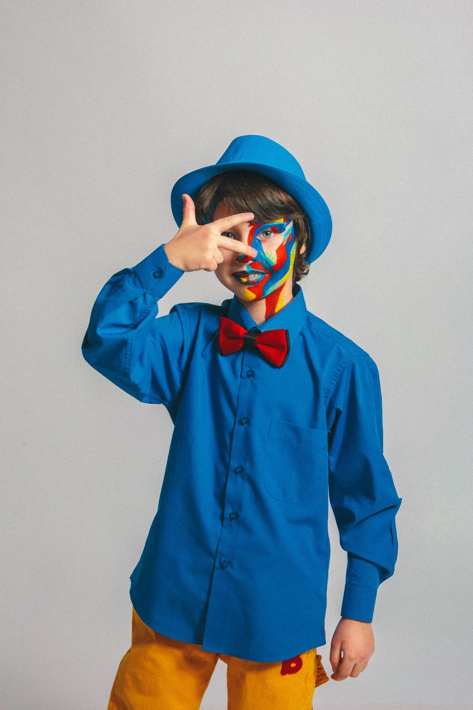 a little boy with a clown face painted on his face, an album cover, inspired by Okuda Gensō, pexels, blue fedora, bow tie, teen boy, dressed in blue