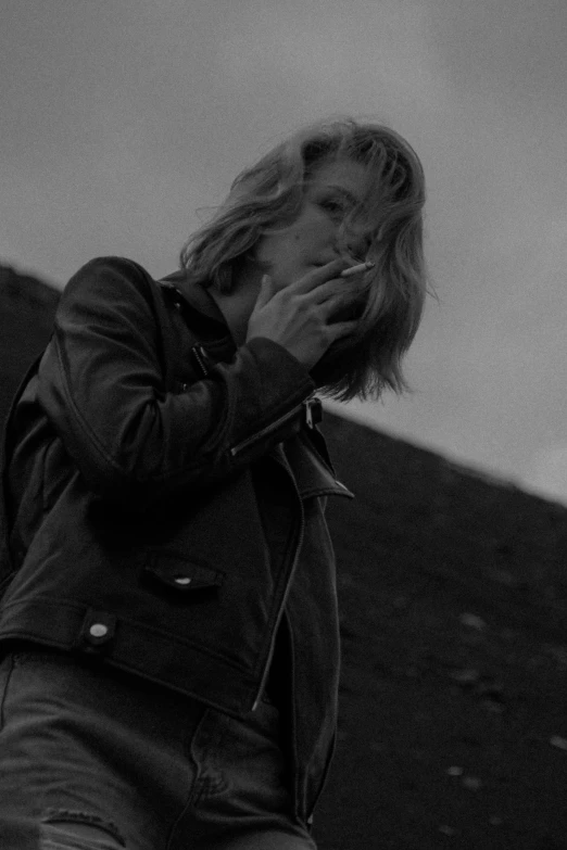 a black and white photo of a woman smoking a cigarette, a black and white photo, inspired by Lasar Segall, tumblr, in an old 1950s leather jacket, at a volcano, leica 8k still from an a24 film, a girl with blonde hair