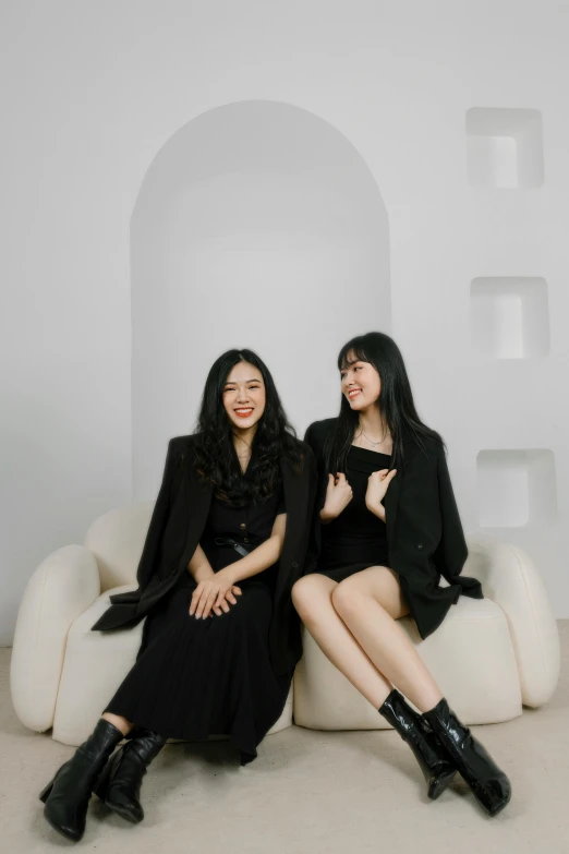 two women sitting next to each other on a couch, an album cover, inspired by Wang Duo, unsplash, wearing causal black suits, jet black hair, in a white room, sisters