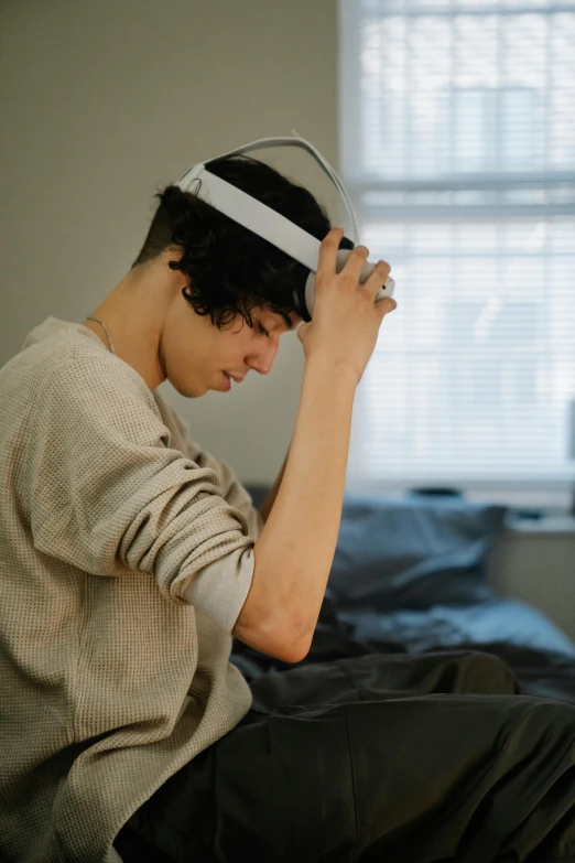 a man sitting on top of a bed next to a window, an album cover, inspired by John Luke, trending on pexels, headphones on his head, frustrated expression, side profile view, brain computer interface