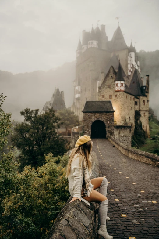 a woman sitting on a wall in front of a castle, by Daniel Lieske, pexels contest winner, 🍂 cute, in a rainy environment, panoramic view of girl, hazy